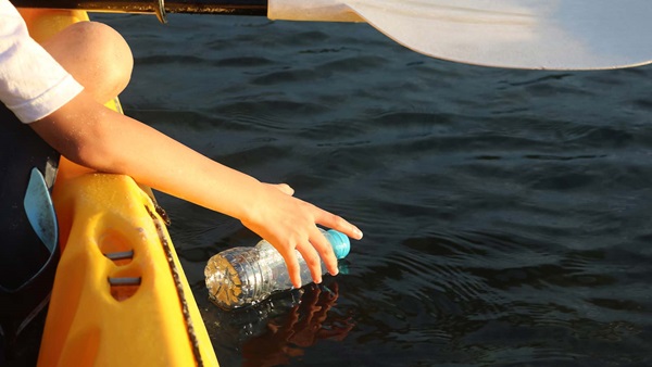 persona raccoglie bottiglia dal mare